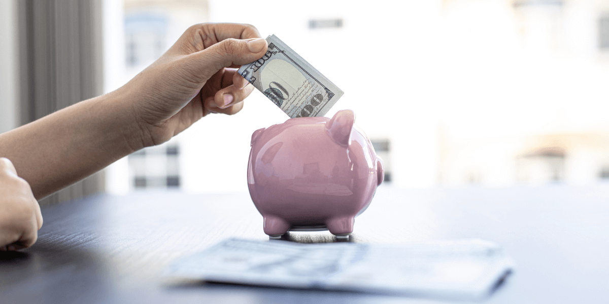 Adding a $100 bill to a pink piggy bank